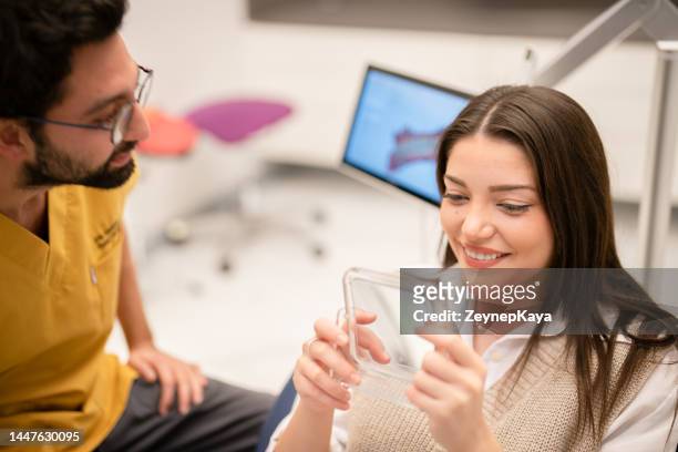 young woman looking at her teeth at mirror, sitting on dentist's chair - 3d scanning stock pictures, royalty-free photos & images