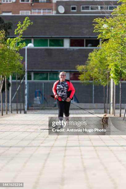 blonde girl with eyeglasses running with her dog down a city street. - cansado 個照片及圖片檔