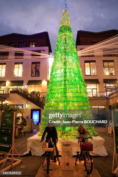 Personnes sur des vélos produisant de l'électricité pour illuminer l'arbre de Noël écologique non végétal constituée de bouteilles plastiques...