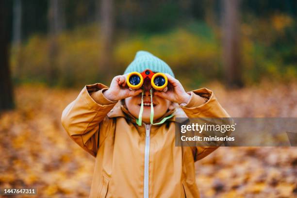 mignonne petite fille tenant de petites jumelles dans les bois - paire de jumelles photos et images de collection