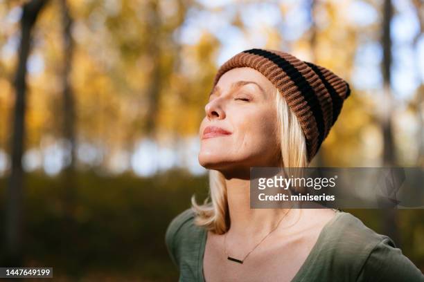 portrait of a beautiful woman standing in the woods enjoying the sunlight - mature woman face beauty stockfoto's en -beelden