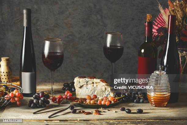 red wine and cheese still life on rustic table with grapes, wine bottles and wine glasses, honey and nuts - roquefort stock pictures, royalty-free photos & images