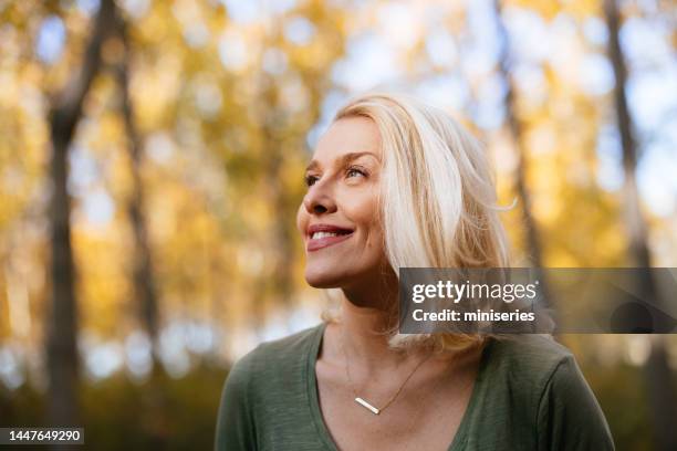 portrait of a beautiful woman standing in the woods enjoying the sunlight - mulheres maduras imagens e fotografias de stock