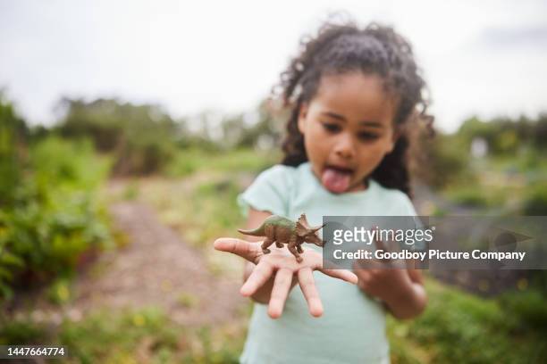 menina segurando um dinossauro de brinquedo em sua mão em um jardim - dinosaur toy i - fotografias e filmes do acervo