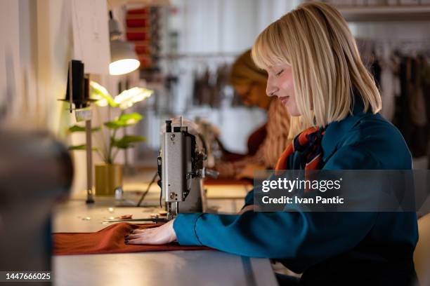 young female tailor working on a sewing machine in a clothing design studio. - sewing stock pictures, royalty-free photos & images