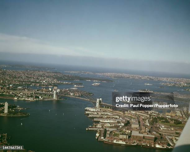 Aerial view looking east of ships moored at wharves with Sydney Harbour Bridge spanning Sydney Harbour in the city of Sydney in New South Wales,...