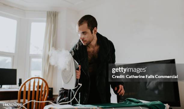 a man wearing a dressing gown irons a green t-shirt - interim stock pictures, royalty-free photos & images