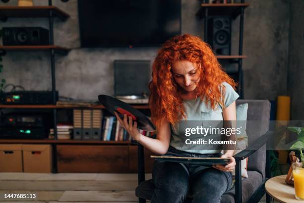 a woman looks at old gramophone records while sitting in the living room of her apartment - collection bildbanksfoton och bilder