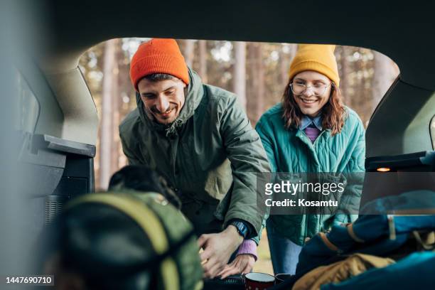 a couple in love take personal belongings from the car trunk while their dog stands in front of them - young men camping stock pictures, royalty-free photos & images
