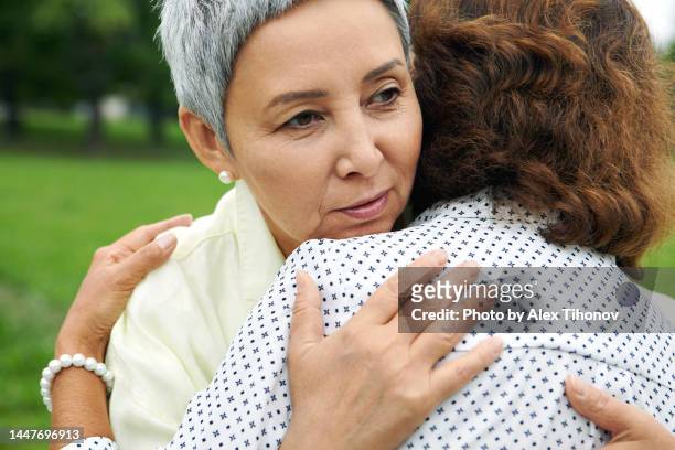 older women hugging, supporting mature friend, close up - mourning stock-fotos und bilder