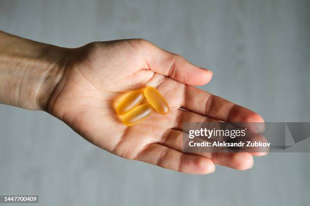 a woman holds omega-3 fish oil capsules in the palm of her hand or in her hand. healthy lifestyle, prevention and treatment of diseases. the girl takes and drinks dietary supplements and vitamins. biologically active additive. intake of healthy fats. - fish oil stock photos et images de collection