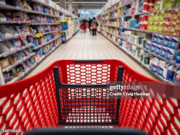 personal perspective of a shopper pushing shopping trolley along product aisle while shopping in a supermarket. super market tinned and canned produce aisle with blurred shelves and products to make it generic. - personal shopper grocery - fotografias e filmes do acervo