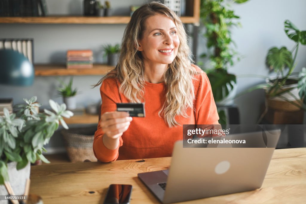 Reife erwachsene Frau, die zu Hause arbeitet (Laptop, Kreditkarte)