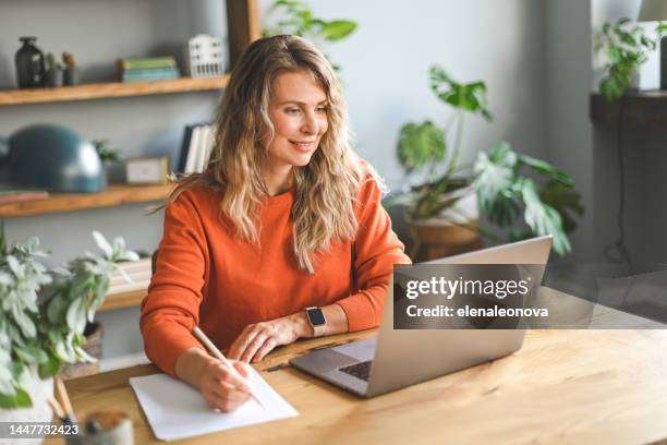 mature adult woman working at home (laptop, mobile phone, document ) - online class stock pictures, royalty-free photos & images