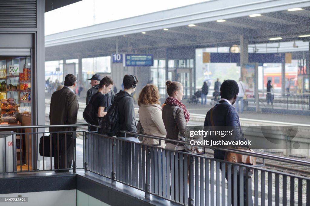 Adults and commuters are waiting and leaning at railing in railroad station Essen