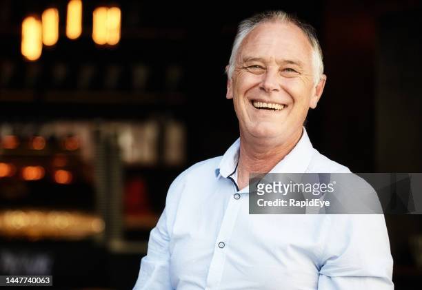 handsome man smiles and laughs as he stands in the entrance of a bar and restaurant: business is good! - powder blue shirt stock pictures, royalty-free photos & images