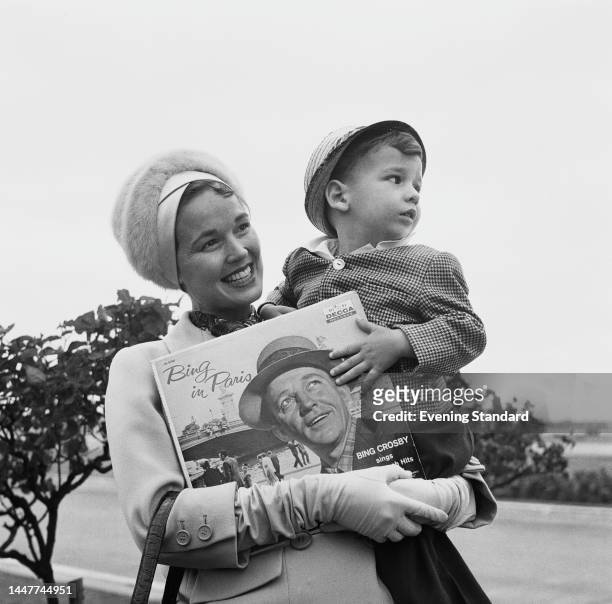 American actress and singer Kathryn Crosby holding son Harry, aged three, and a copy of husband Bing Crosby's album 'Bing in Paris' during a visit to...