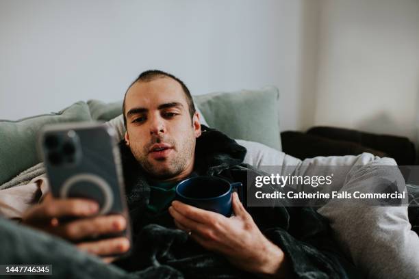 a man relaxes in a bathrobe, while holding a mobile phone - sillón reclinable tipo de silla fotografías e imágenes de stock