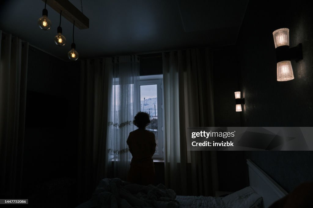 Mature woman is exercising next to the window in the dark bedroom