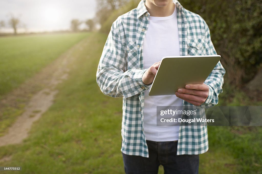 Man walking in countryside and using tablet.