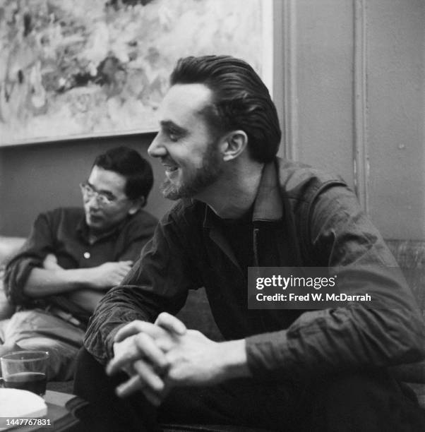 American writer Lew Welch smiles as he sits on a couch in the apartment of photographer Fred McDarrah and his soon-to-be wife, Gloria, New York, New...