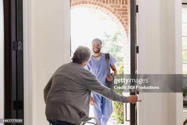 senior man with walker opens door for physical therapist - home carer stock pictures, royalty-free photos & images