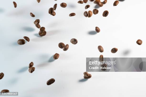 roasted coffee beans flying in mid air in white background - coffee slow motion stock pictures, royalty-free photos & images