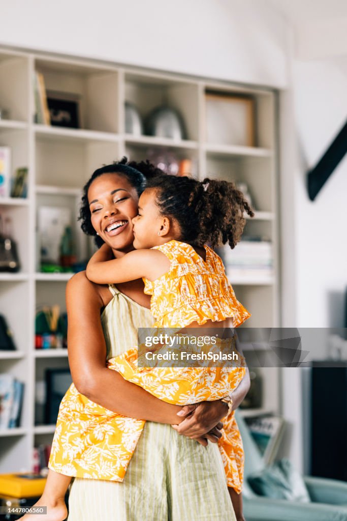 A Beautiful Cute Girl Hugging And Kissing Her Smiling Mother While She Is Holding Her