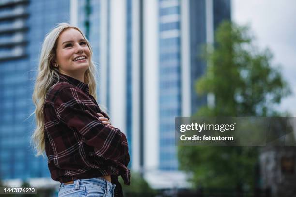 jeune femme debout, les bras croisés, levant les yeux, souriant et réfléchissant - blonde fille photos et images de collection