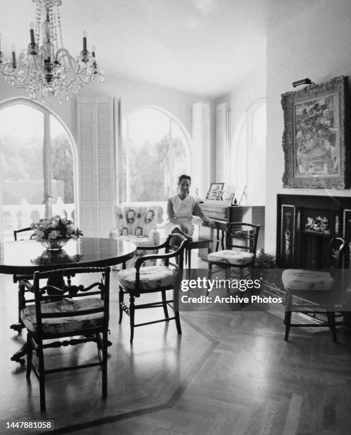 British actress Merle Oberon sitting at a piano, beyond a circular dining table and chairs in her Beverly Hills home, California, circa 1967.