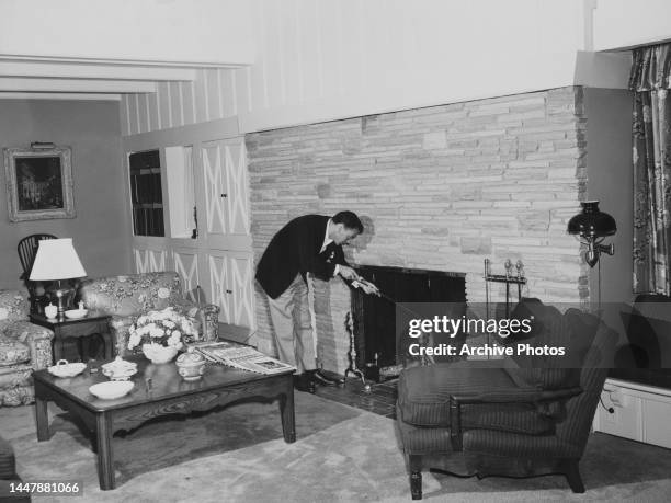 American singer and actor Frank Sinatra stoking the fireplace in the living room of his home, United States, circa 1950.