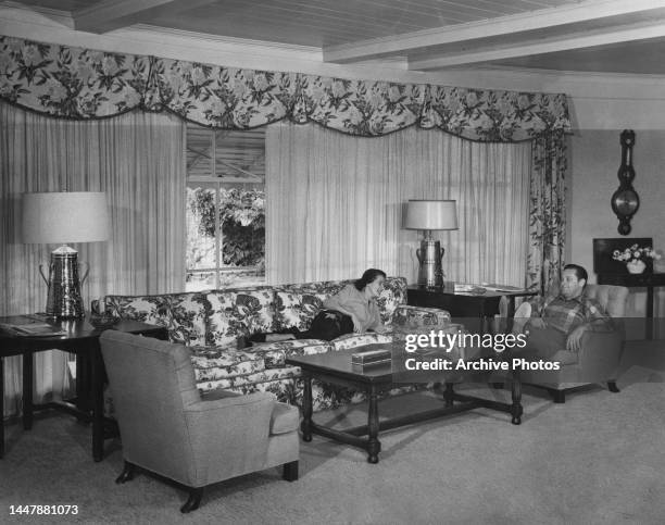 American actress Brenda Marshall reclining on a sofa with her husband, American actor William Holden with his feet on the coffee table before his...