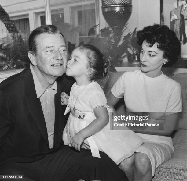 American actor John Wayne gets a kiss on the cheek from his daughter, Marisa Wayne, as his wife, Peruvian actress Pilar Pallete looks on at the...