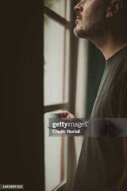 close-up profile of a man standing by a window drinking a cup of coffee - masculinidade imagens e fotografias de stock