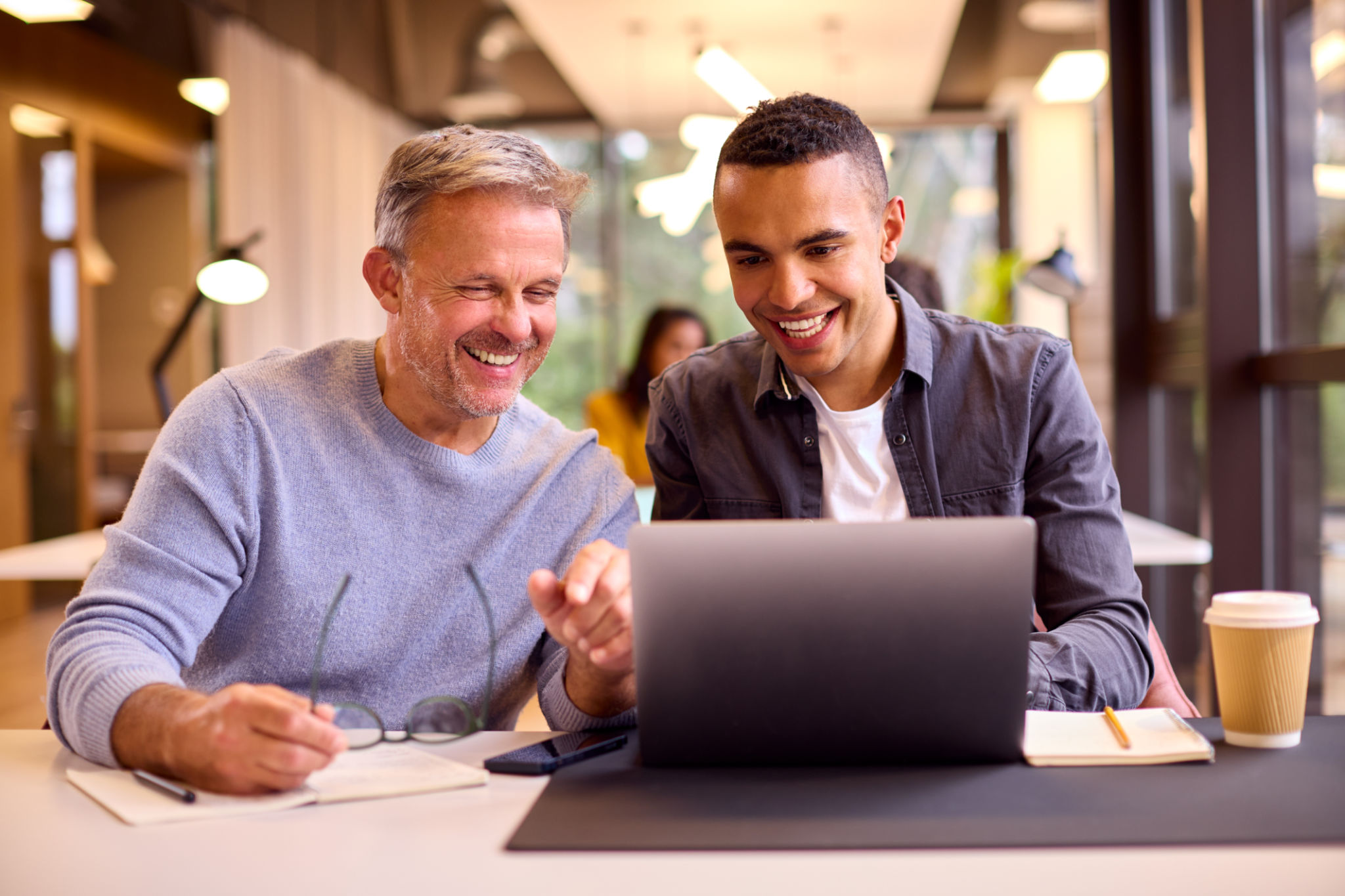 Mature Businessman Mentoring Younger Colleague Working On Laptop At Desk Mature Businessman Mentoring Younger Colleague Working On Laptop At Desk