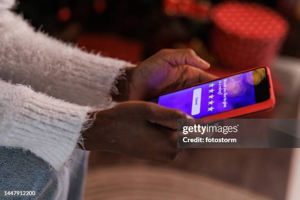 foto recortada de una mujer haciendo compras navideñas en línea a través de un teléfono inteligente - calificación fotografías e imágenes de stock