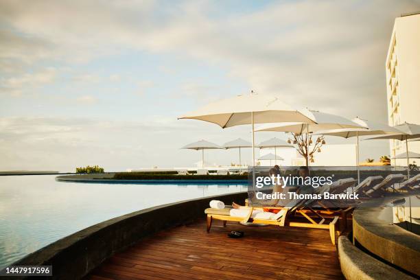 wide shot of woman working on laptop in lounge chair by pool at resort - lugar turístico fotografías e imágenes de stock