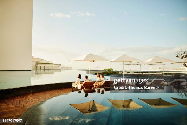 wide shot of family hanging out on lounge chairs by pool at resort - hotel de lujo fotografías e imágenes de stock