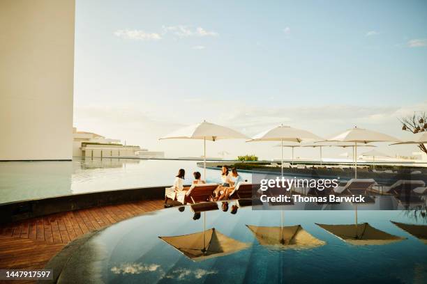 wide shot of family hanging out on lounge chairs by pool at resort - public building stock photos et images de collection