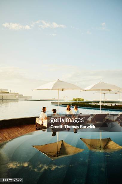 wide shot of family hanging out on lounge chairs by pool at resort - luxury family stockfoto's en -beelden