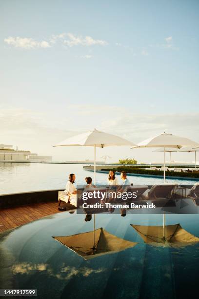 wide shot of family hanging out on lounge chairs by pool at resort - family holidays hotel stock pictures, royalty-free photos & images