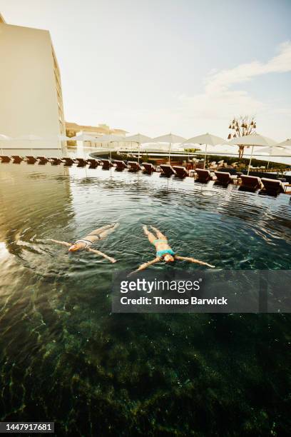 Wide shot of sisters floating on backs in pool at tropical resort