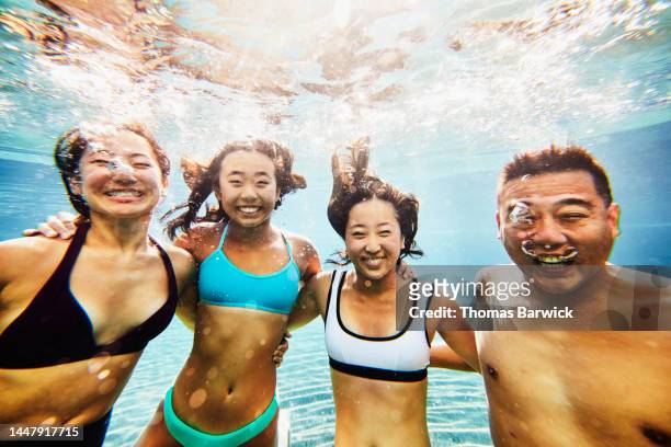 Medium shot of smiling family underwater in pool at tropical resort