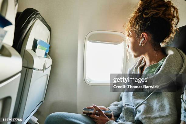 medium shot of girl looking out window of commercial airplane - airplane flying foto e immagini stock