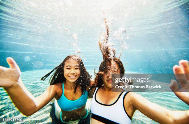 medium shot of smiling sisters underwater in pool at tropical resort - achttien jaar stockfoto's en -beelden