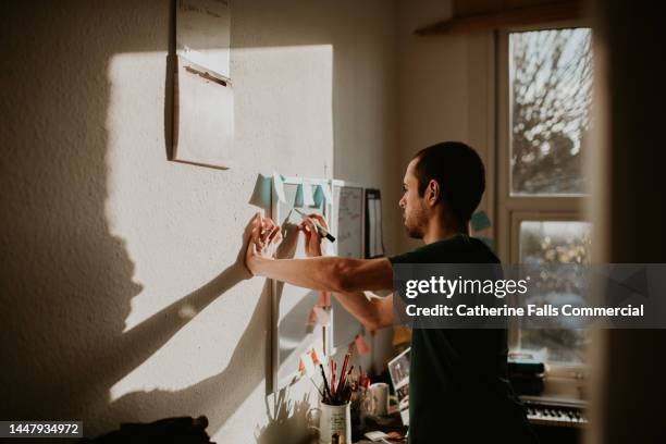 an organised man in a small home-office writes reminders on a wall-mounted white board - office small business stock pictures, royalty-free photos & images