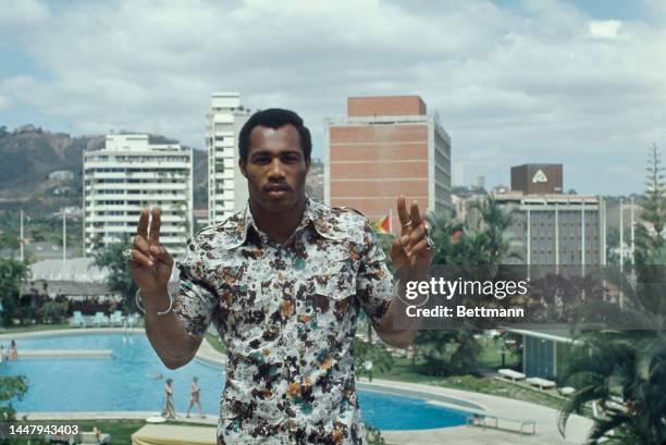 American boxer Ken Norton , wearing a short-sleeve floral pattern shirt, with both hands raised giving the the 'V' for victory symbol on the day of...