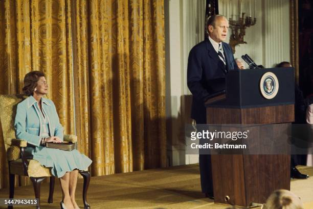 American First Lady of the United States Betty Ford sits with a copy of the bible on her lap watching as her husband Gerald Ford delivers his address...