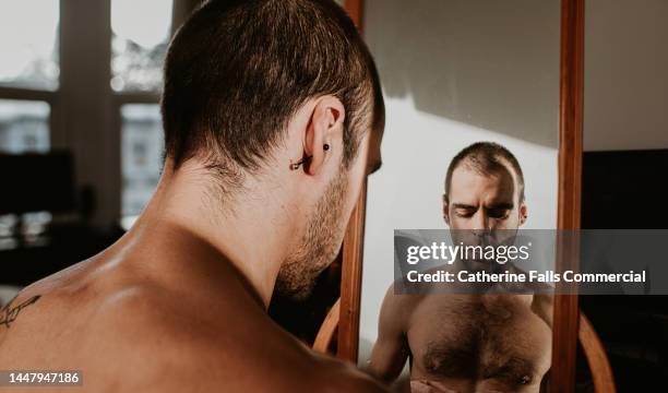 a man looks worried and anxious as he averts his eyes from his own reflection - weight gain foto e immagini stock