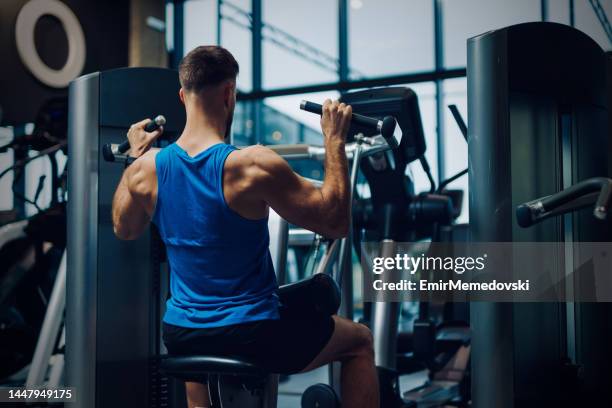 ジムでフィットネスマシンを使って運動する筋肉質の男性ボディービルダー - フィットネスマシン ストックフォトと画像